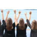 Neljä naista järven rannalla, selin ja kädet ylhäällä