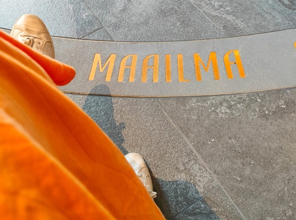 Oranssipukuisen henkilön kenkä lattialla, jossa lukee sana maailma.