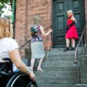 Kolme vammaista henkilöä kirkon portailla, mm. pyörätuoli.
